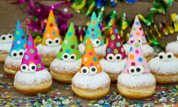 Mehrere Berliner mit Augen und bunten Hüten liegen auf Konfettidekoration