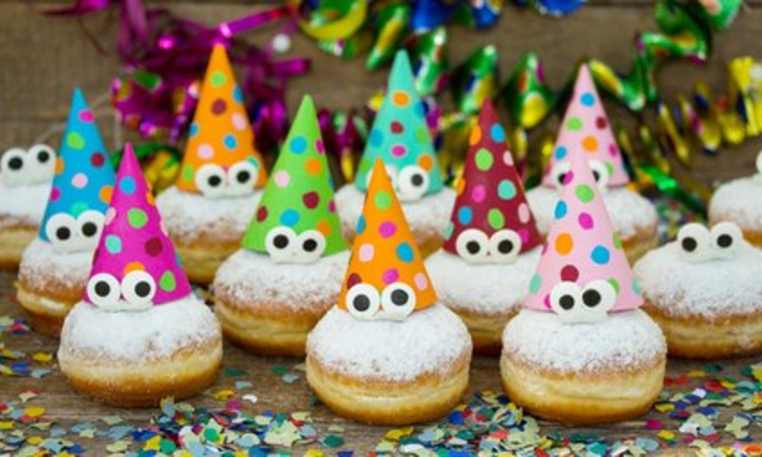 Mehrere Berliner mit Augen und bunten Hüten liegen auf Konfettidekoration