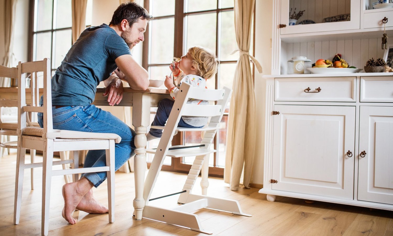 Ein junger Mann und ein Kleinkind im Hochstuhl sitzen gemeinsam am Esstisch