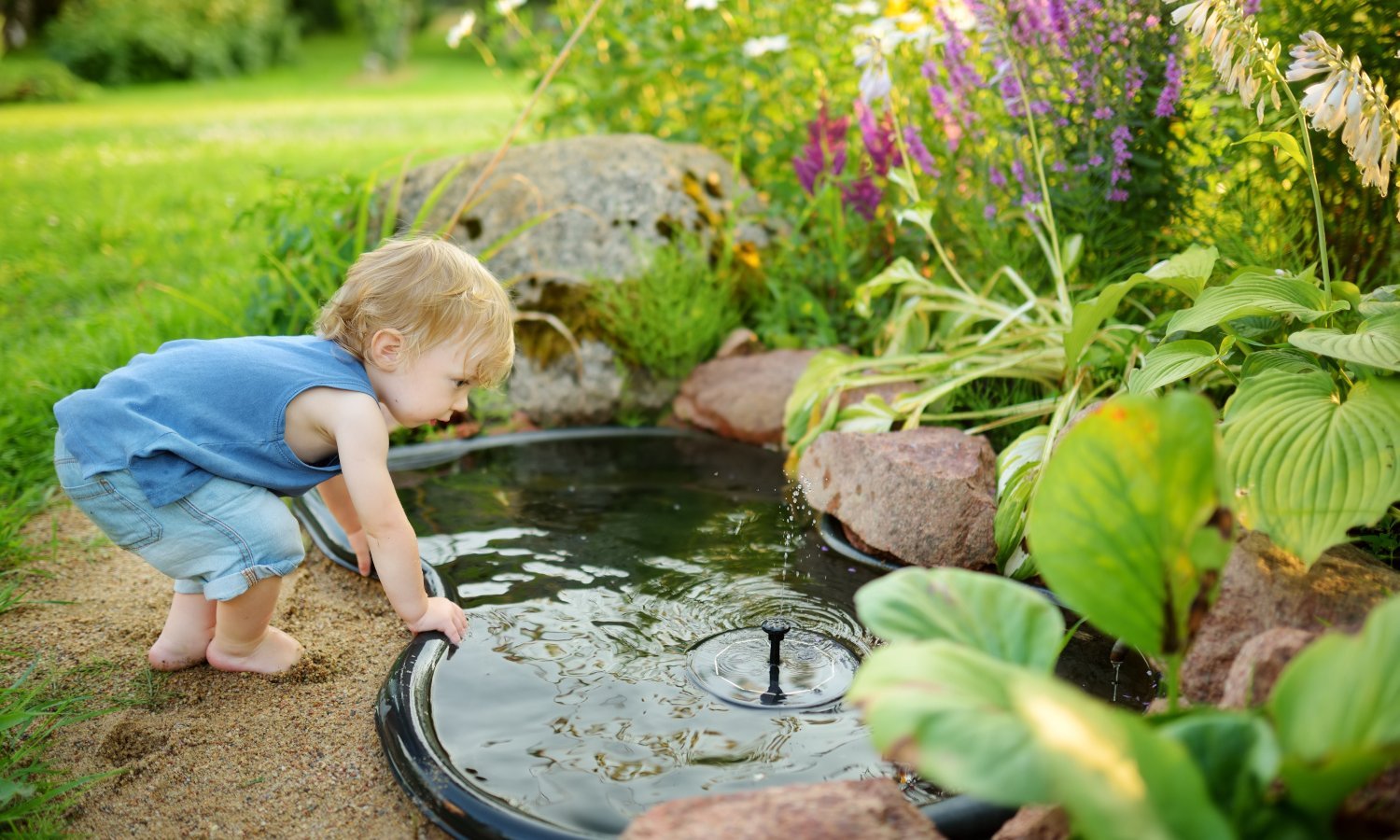 Ein Kleinkind stützt sich mit den Händen am Rand des Gartenteichs ab