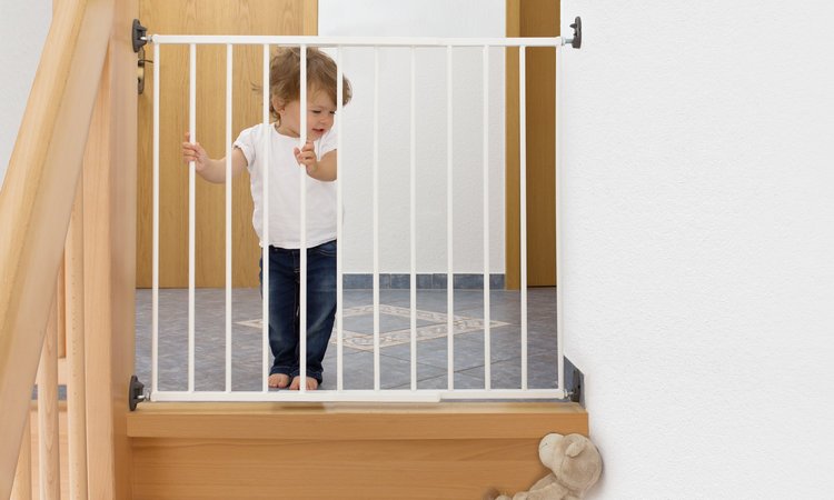 Ein Kleinkind steht vor einem mit Treppengitter gesicherten Treppenabgang