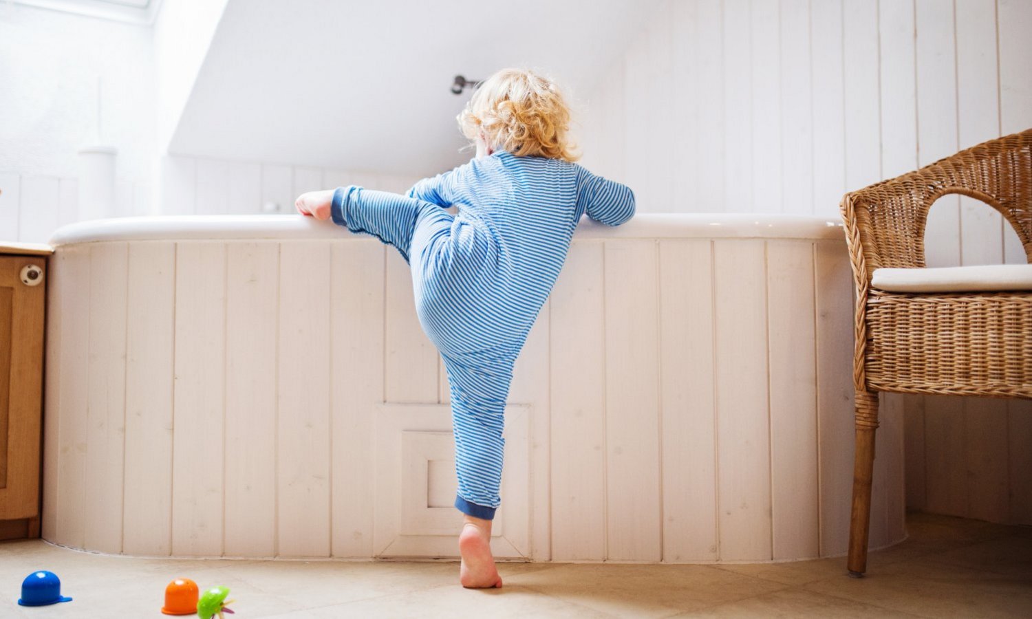 Ein Kleinkind klettert in die Badewanne im lichtdurchfluteten Badezimmer