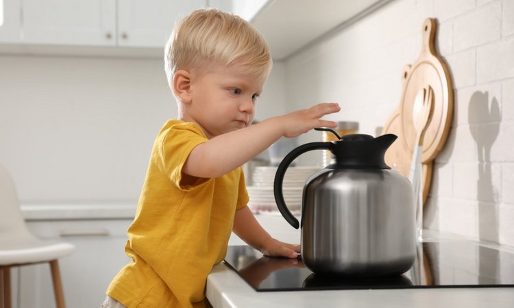 Ein Kind greift nach einer Thermoskanne auf dem Herd