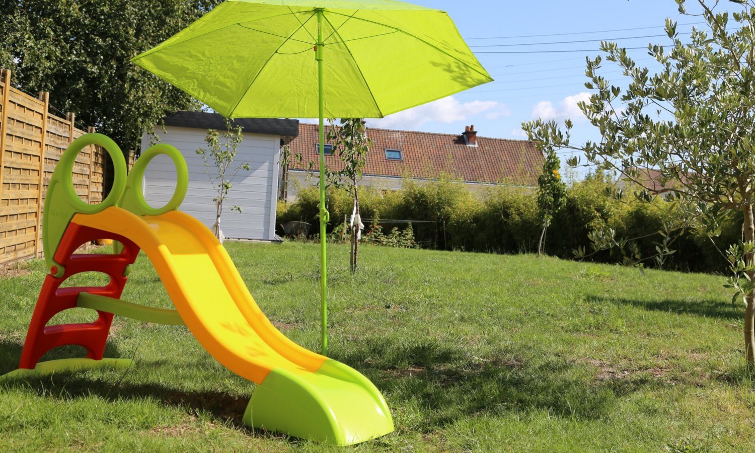Eine bunte Plastikkinderrutsche im Garten wird durch einen Sonnenschirm geschützt