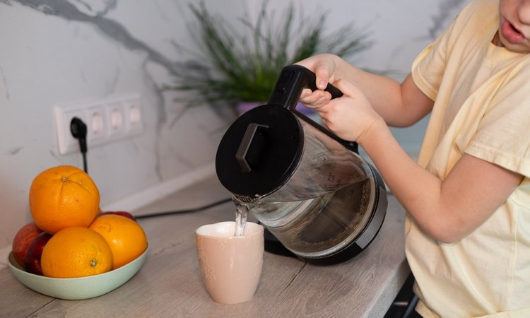 Kind gießt heißes Wasser aus dem Wasserkocher in eine Tasse