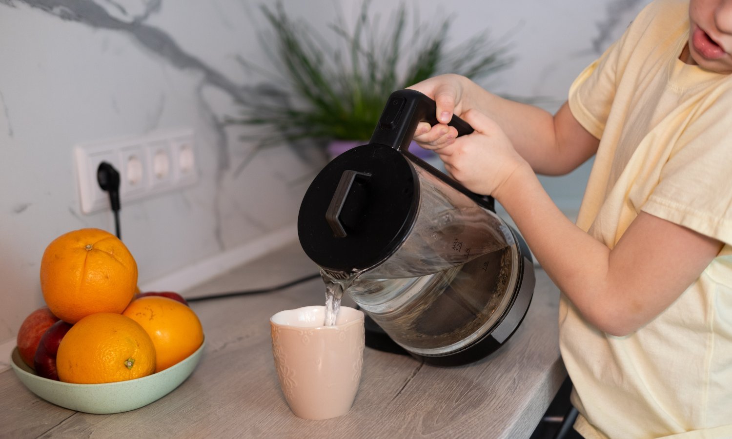 Kind gießt heißes Wasser aus dem Wasserkocher in eine Tasse