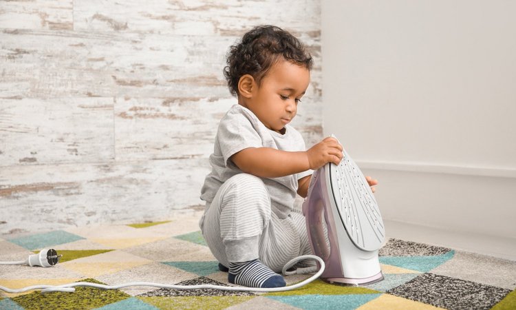 Ein Kleinkind fasst auf die Bügelfläche eines ausgesteckten Bügeleisens