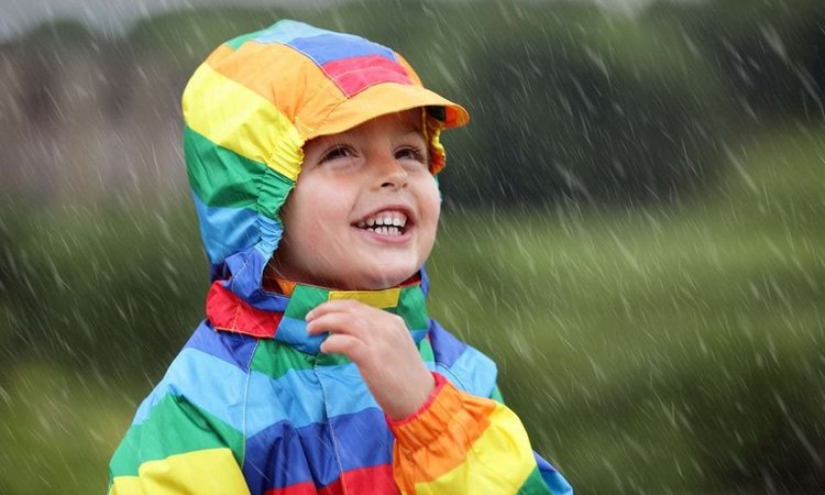 Ein Kind mit bunter Regenjacke steht lächelnd im Regen