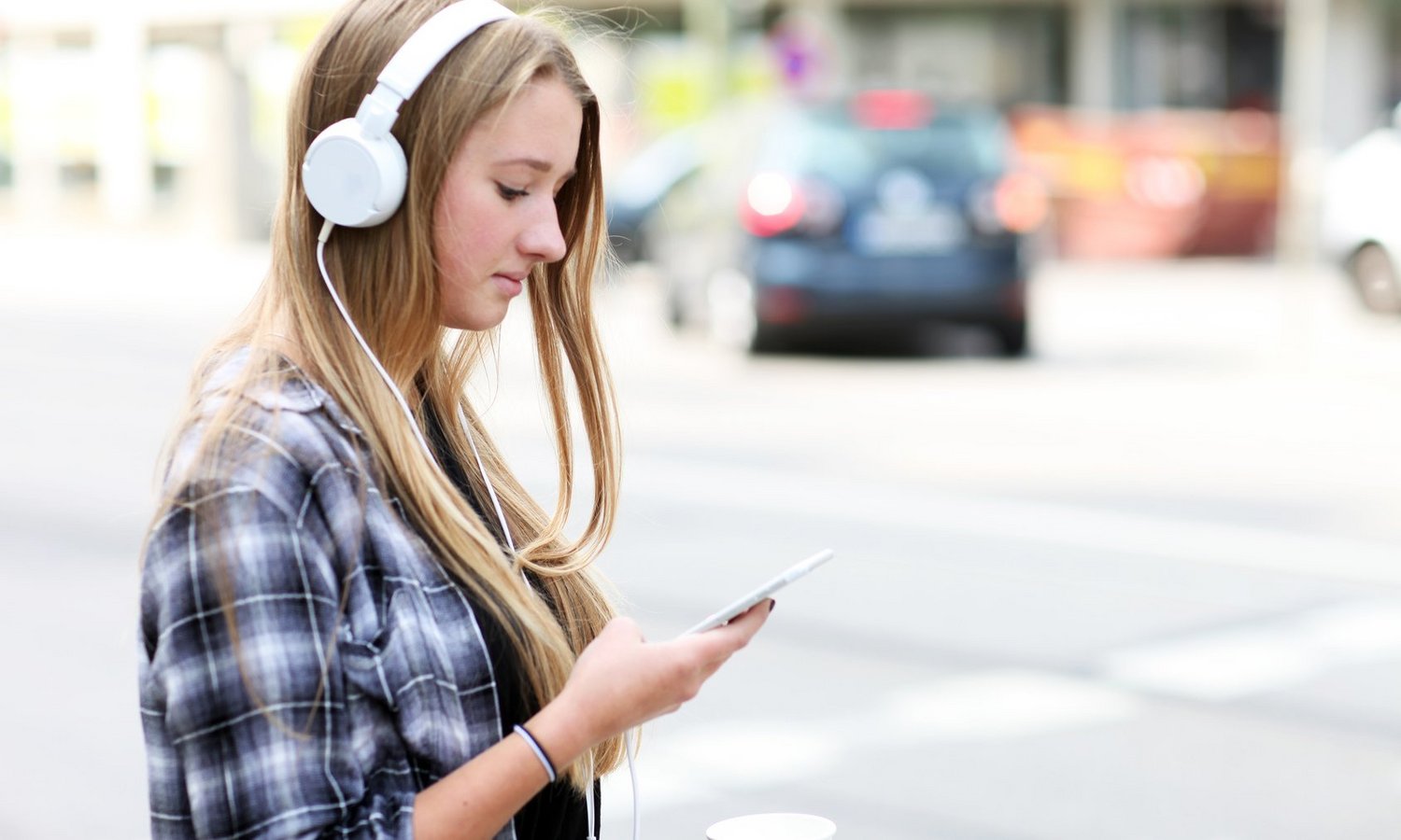 Mädchen mit Kopfhörern schaut im Straßenverkehr auf ihr Handy