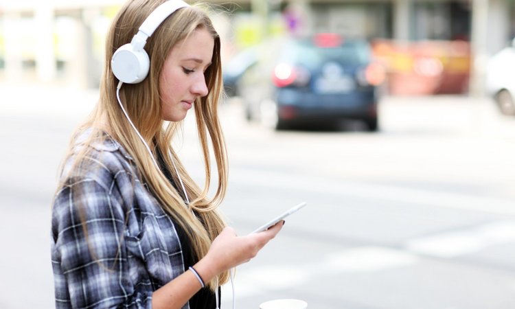 Mädchen mit Kopfhörern schaut im Straßenverkehr auf ihr Handy