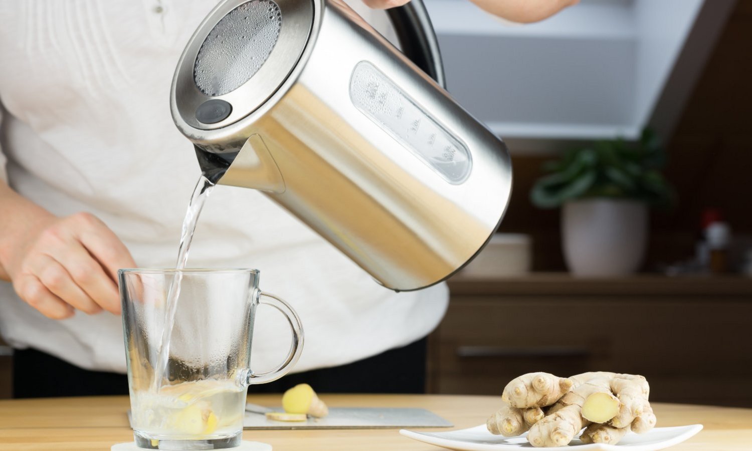 Jemand gießt eine Tasse Ingwertee mit heißem Wasser aus dem Wasserkocher auf
