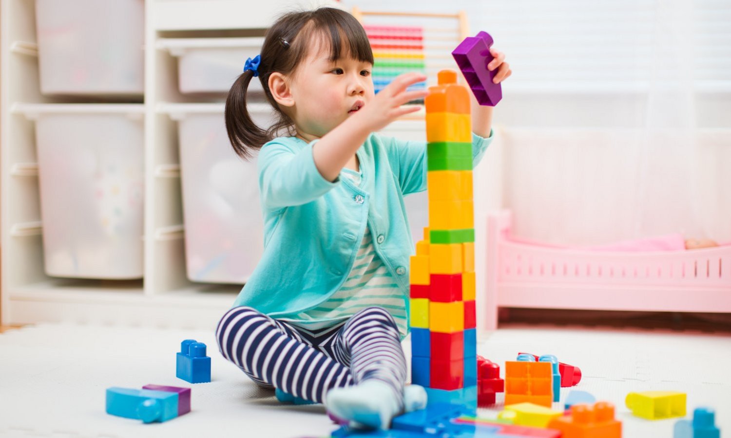 Ein Kleinkind baut auf dem Boden sitzend einen Turm aus bunten Bauklötzen