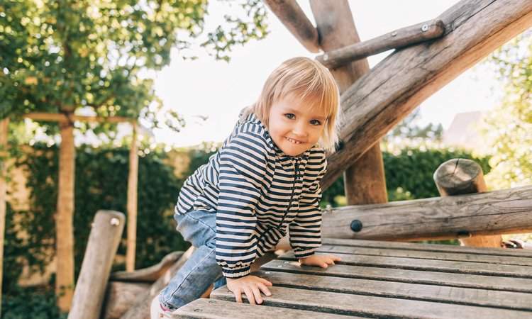 Ein blondes Mädchen klettert auf einem Holzklettergerüst und schaut in die Kamera