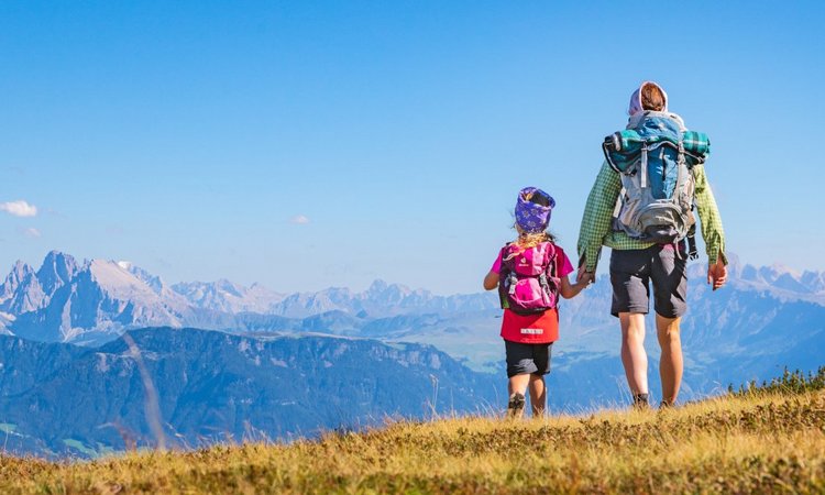 Eine Frau und ein Kind in Wanderkleidung stehen bei klarem Wetter auf dem Bergwipfel und blicken auf eine Gebirgskette