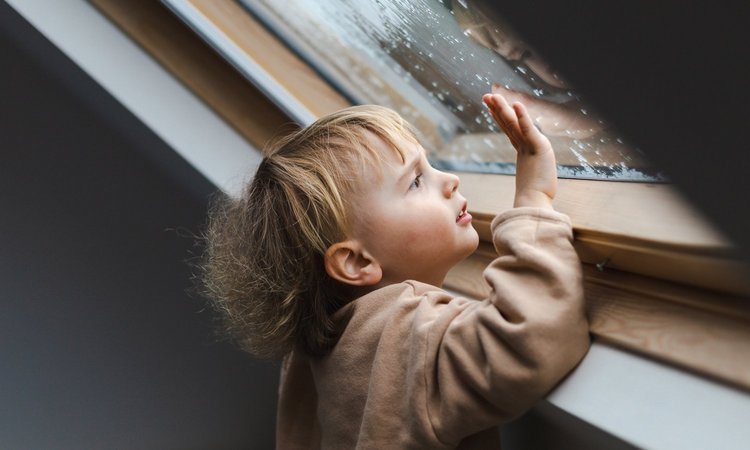 Ein Kleinkind schaut bei Regen aus dem Dachfenster