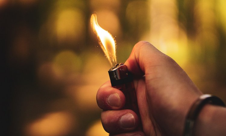 Eine Hand hält ein Feuerzeug mit offener Flamme