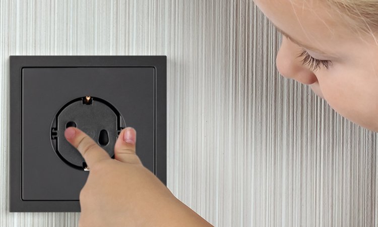Ein Kind fasst in eine mit Kindersicherung gesicherte Steckdose