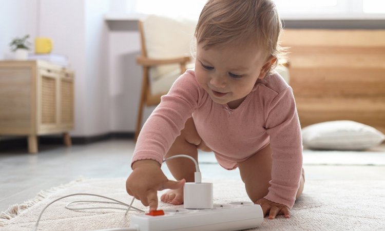 Ein Kleinkind spielt auf dem Boden mit einer Mehrfachsteckdose
