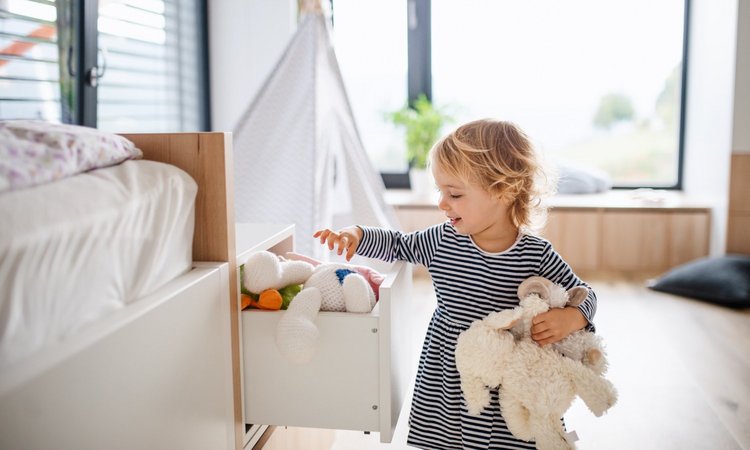 Ein Kleinkind räumt Stofftiere aus einer Schublade im lichtdurchfluteten Kinderzimmer