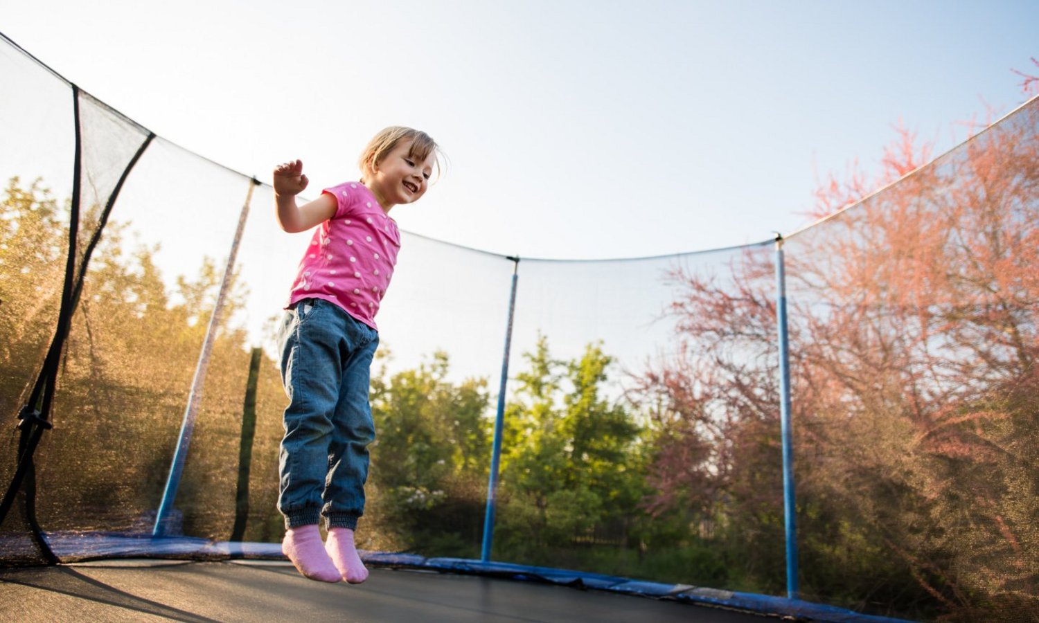 Ein Kind springt gut gelaunt Trampolin im Garten