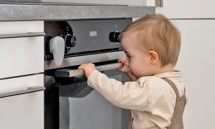 Ein Kind steht an einer gesicherten Backofentür