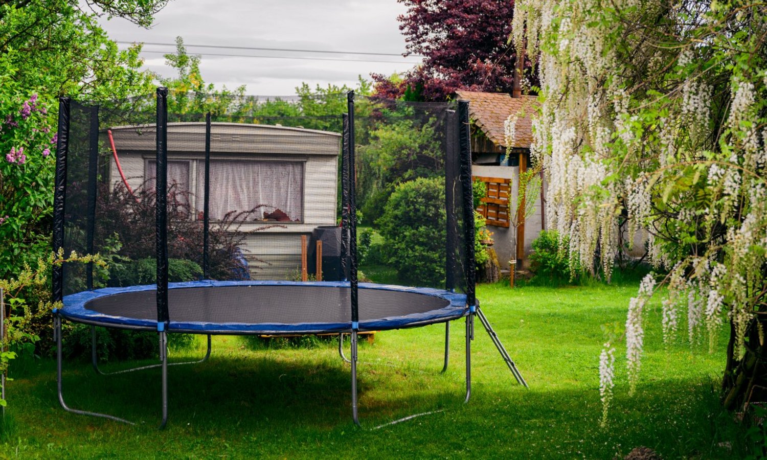 Ein großes Trampolin steht zwischen Bäumen auf der Wiese im Garten