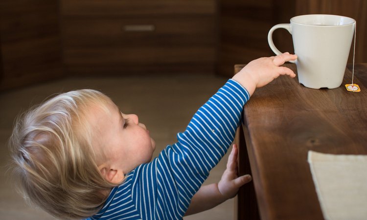 Ein Kleinkind greift nach einer Tasse Tee auf dem Tisch