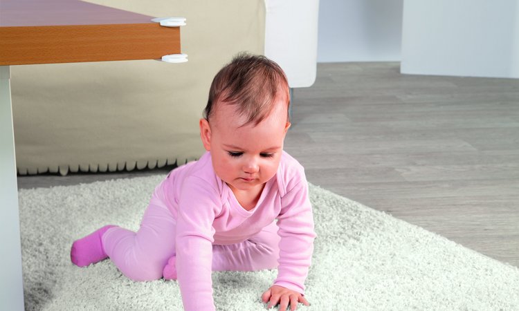 Ein Kind krabbelt auf dem Teppich neben einem Tisch