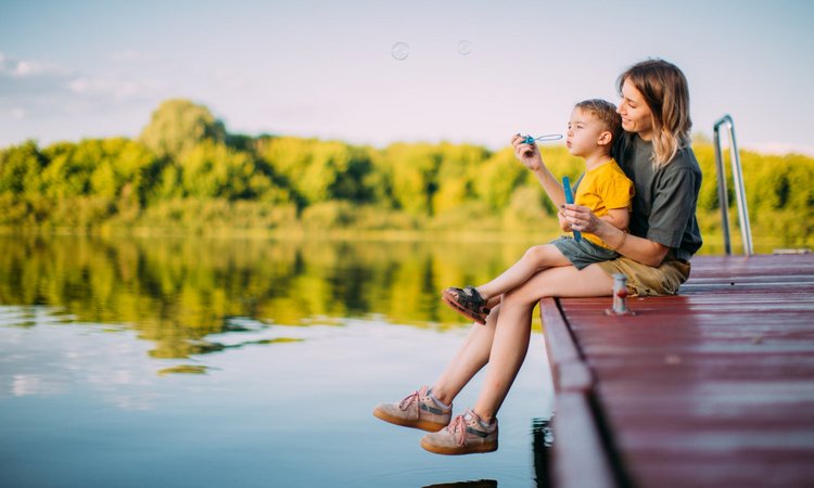 Eine Frau und ein Kind sitzen am Steg eines Sees und blasen Seifenblasen