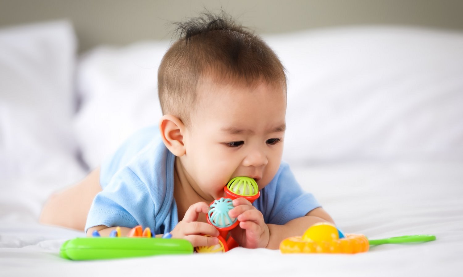 Liegendes Baby nimmt Spielzeug in den Mund