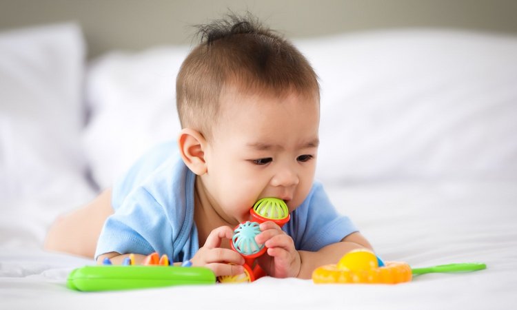 Liegendes Baby nimmt Spielzeug in den Mund