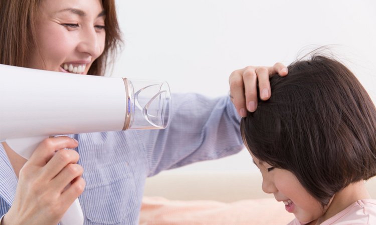 Eine Frau föhnt einem Mädchen lächelnd die Haare