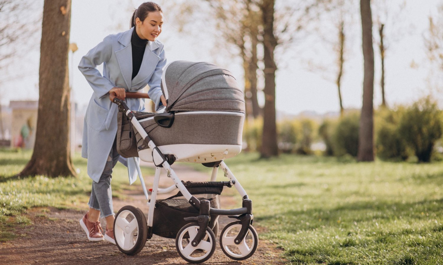 Eine Frau schaut beim Spaziergang im Grünen in den Kinderwagen