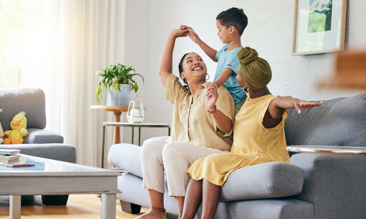 Zwei Frauen sitzen auf einer Couch im Wohnzimmer und ein Kind steht hinter ihnen auf der Couch