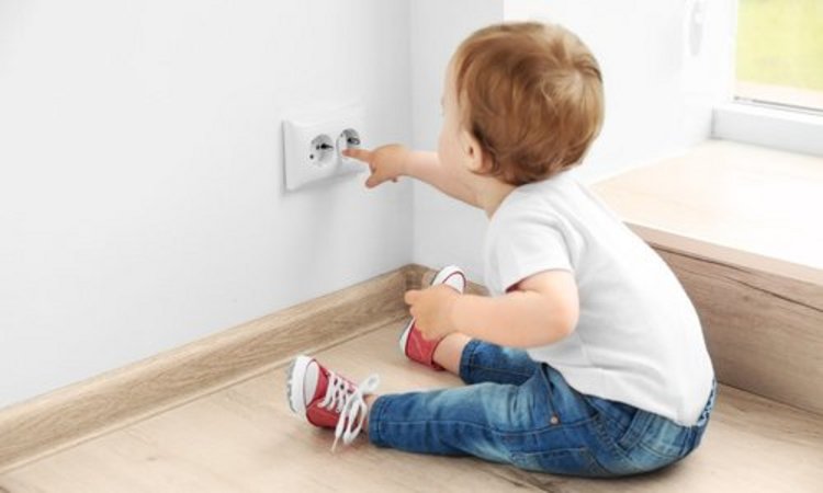 Ein Kleinkind sitzt auf dem Boden und spielt mit dem Finger an einer Steckdose rum