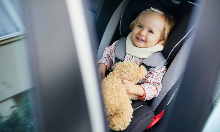 Ein Kleinkind sitzt im Auto in einem Kindersitz und hält einen Teddy fest