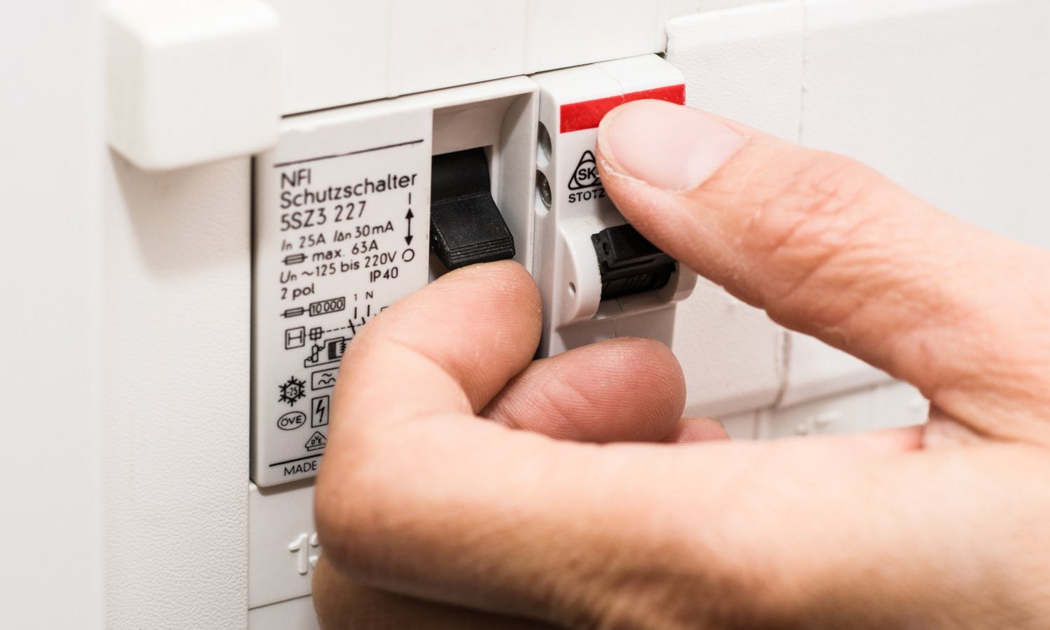 Eine Hand schaltet einen FI-Schalter