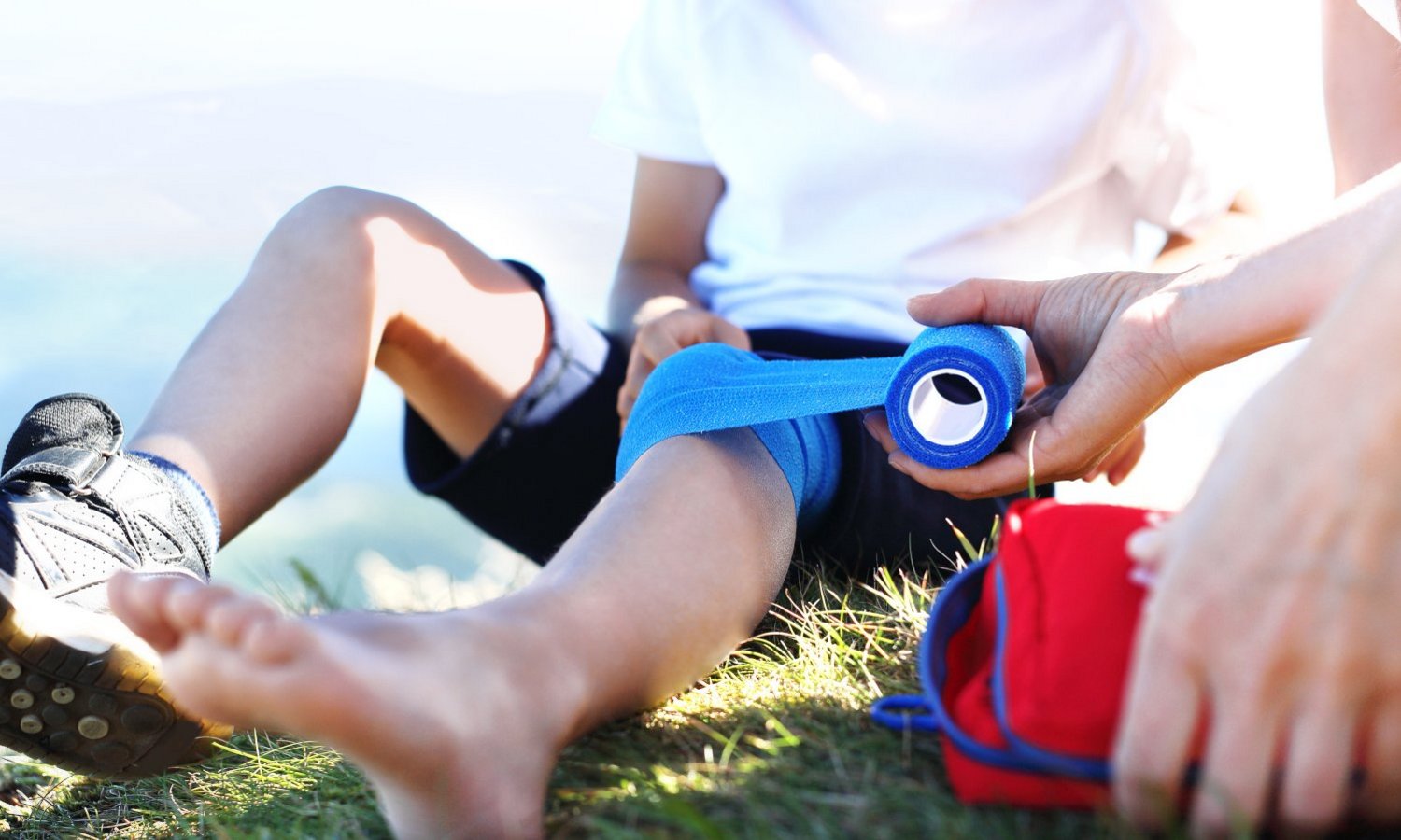 Ein Erwachsener verbindet einem Kind das verletzte Knie mit einem blauen Verband