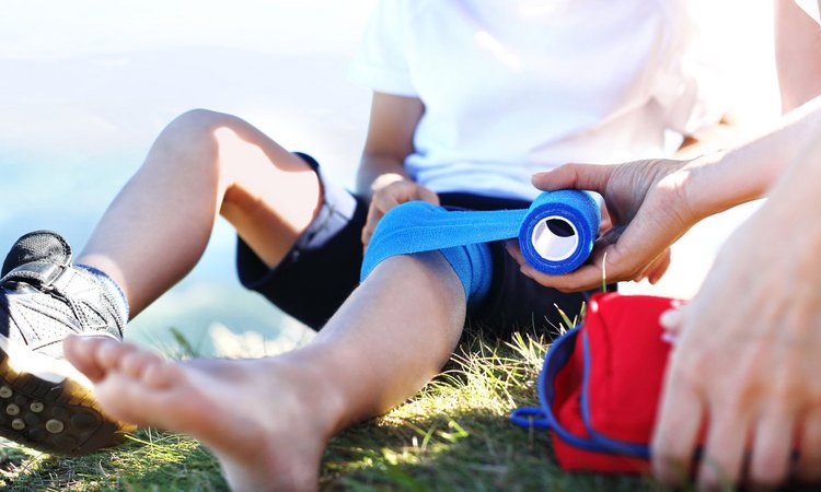 Ein Erwachsener verbindet einem Kind das verletzte Knie mit einem blauen Verband