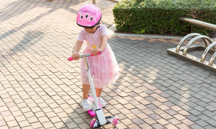 Ein in rosa gekleidetes Kleinkind mit Helm fährt auf einem Scooter