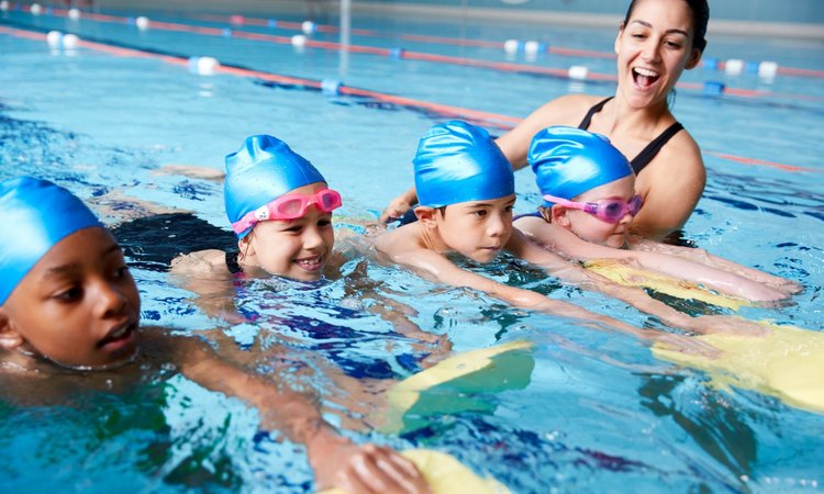 Vier Kinder mit Schwimmbrettern erhalten von einer Lehrerin Schwimmunterricht