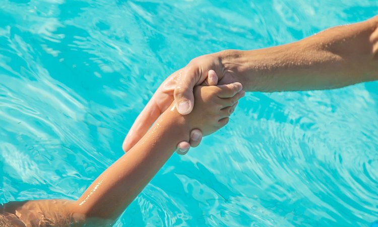 Erwachsener zieht Kind an der Hand aus dem Wasser