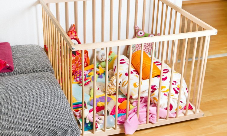 Ein Laufstall mit bunten Kissen und Kuscheltieren und Spielzeug