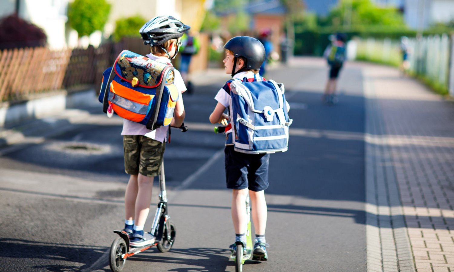 Zwei Kinder mit Schulranzen fahren mit dem Roller zur Schule