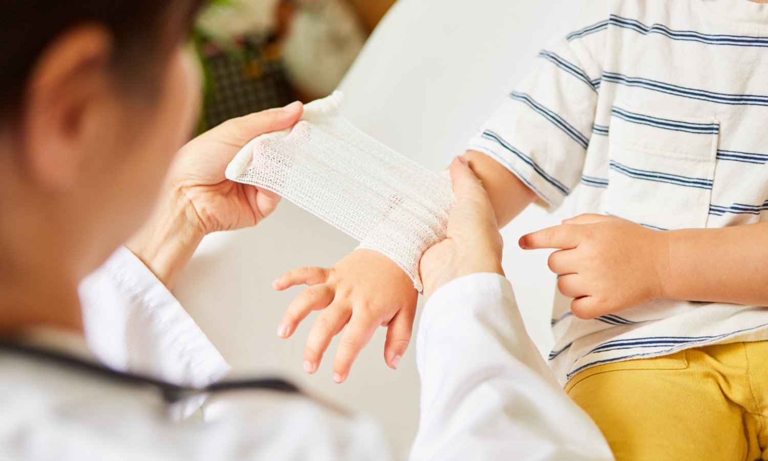 Kind bekommt den Arm mit einem Verband verbunden