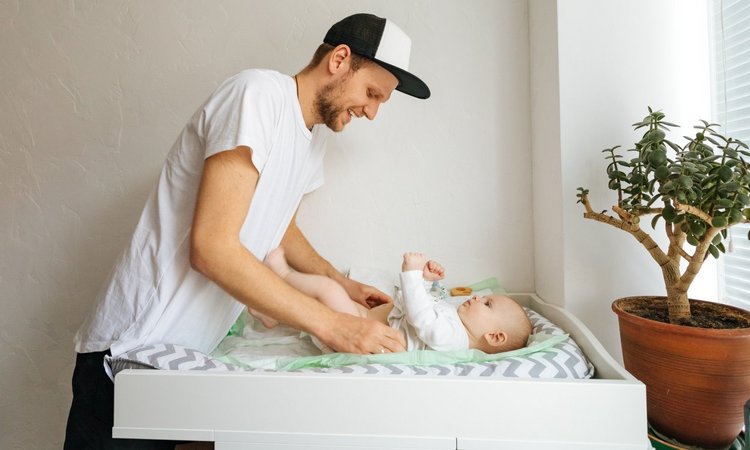 Junger Mann wickelt ein Baby auf dem Wickeltisch