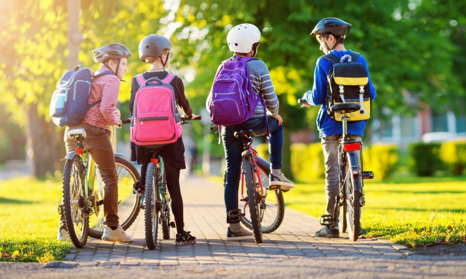 Vier Kinder auf Fahrrädern fahren mit dem Rad durch den Park zur Schule