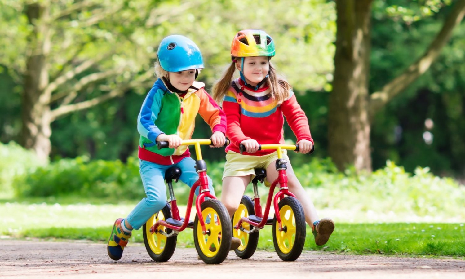 Zwei Kleinkinder mit Helm fahren Laufrad durch den Park