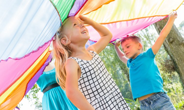 Ein Mädchen steht in der Mitte unter einem von anderen Kindern hochgehaltenen Schwungtuch