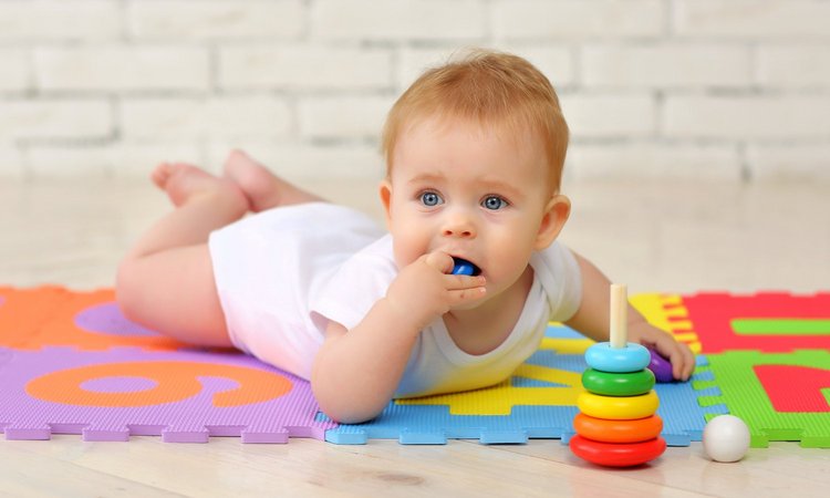 Ein bäuchlings liegendes Baby nimmt buntes Plastikspielzeug in den Mund